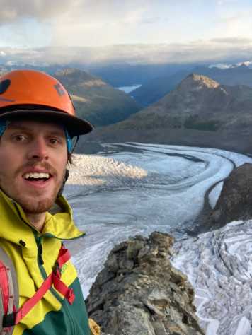 picture of janic cathomen wearing an orange helmet and with a view on a glacier